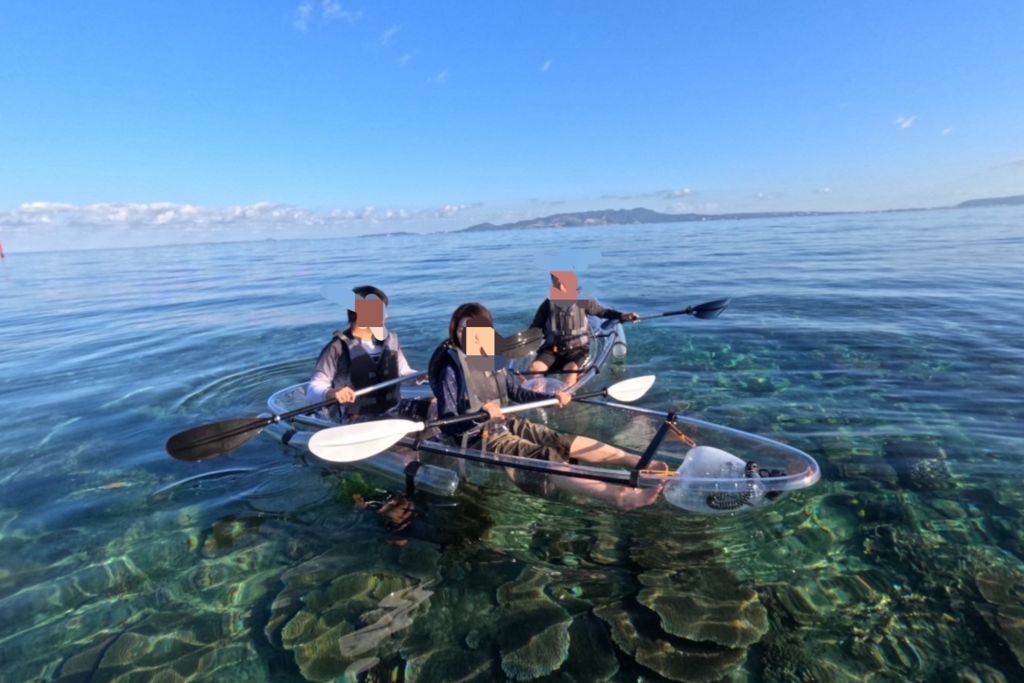 宮古島のクリスタルクリアな海でサンゴ礁の上をクリアカヤックで楽しむカップルと一人の男性