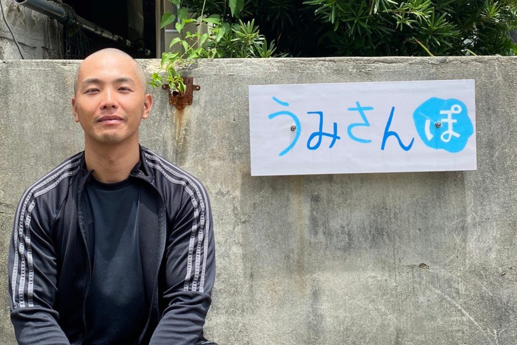 うみみんぽの看板の前で写真を撮る坊主の男性、ハゲではない