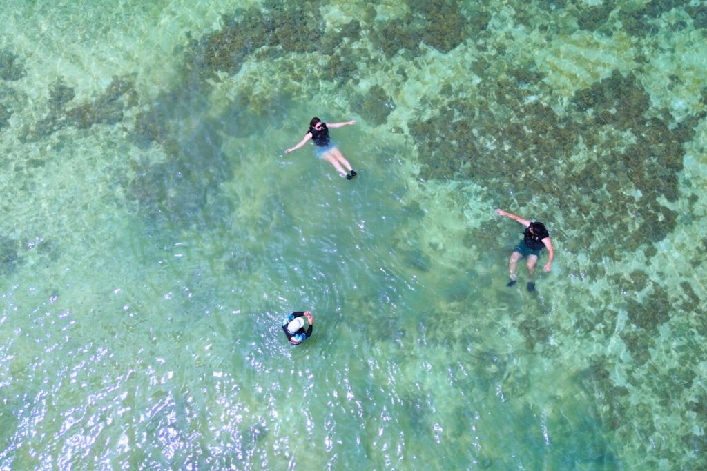 ビーチの浅瀬で浮いている三人をドローンで撮影した写真