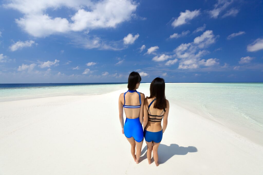 ユニの浜を歩く水着女性二人を後ろから撮影した写真