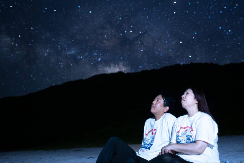 星空を見上げながらたそがれる二人 背景にはきれいな天の川
