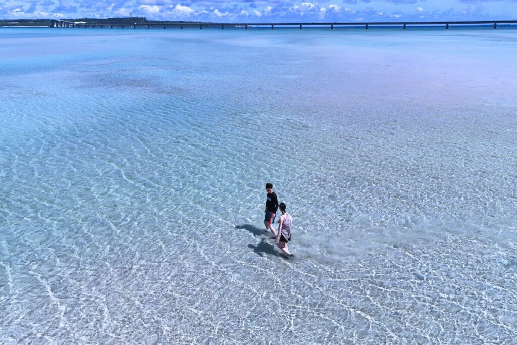 輝く海の上を歩く二人 奥には伊良部大橋が映る