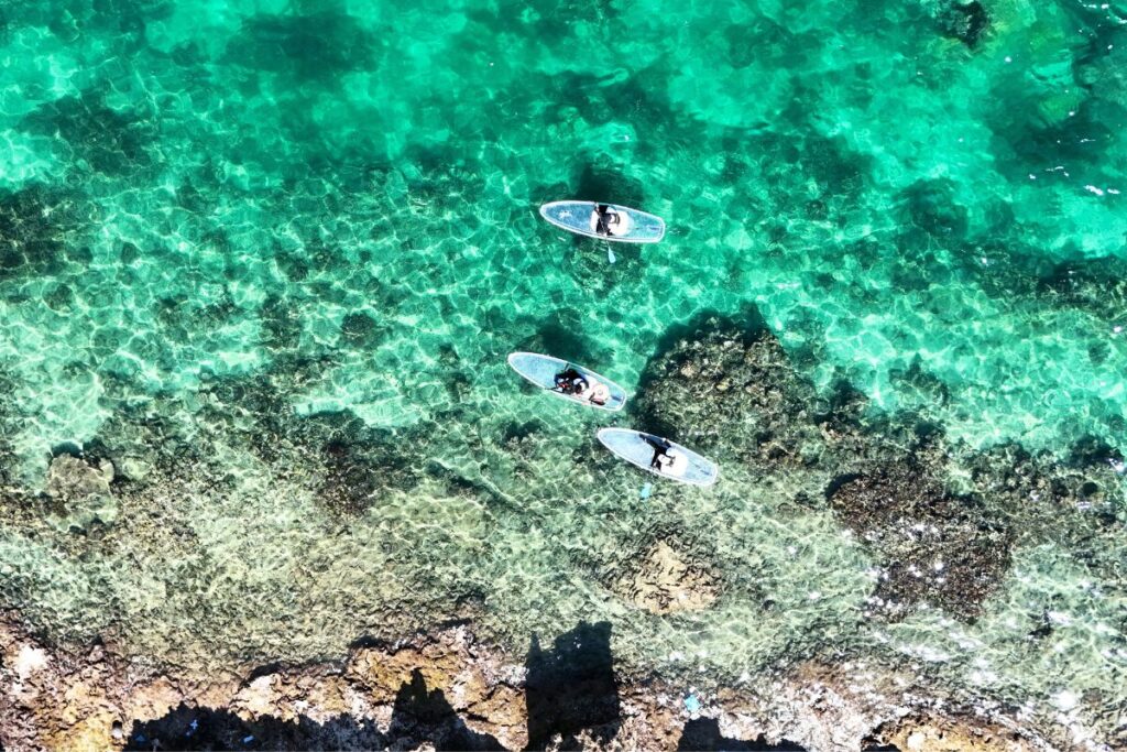 エメラルドグリーンの海の上を漕ぐ3人 ゴツゴツした岩場もいい味を出している