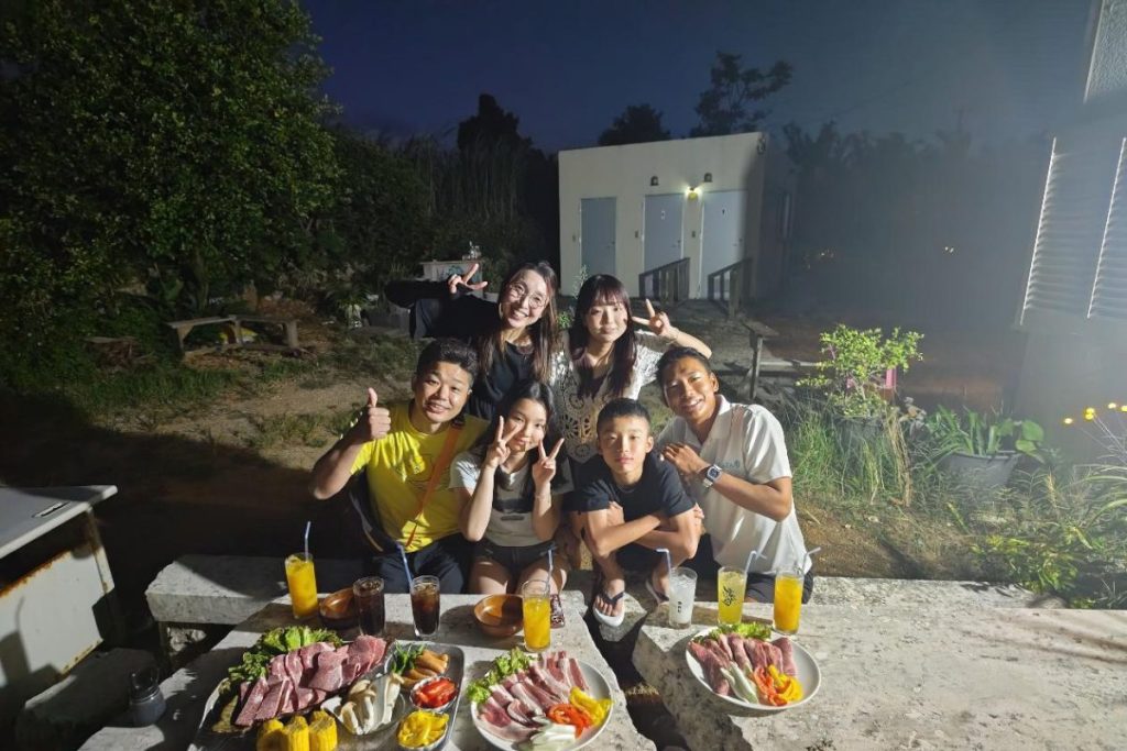 宮古島の一日アテンドツアーで、家族とガイドが夜の屋外BBQを囲んで記念撮影する様子