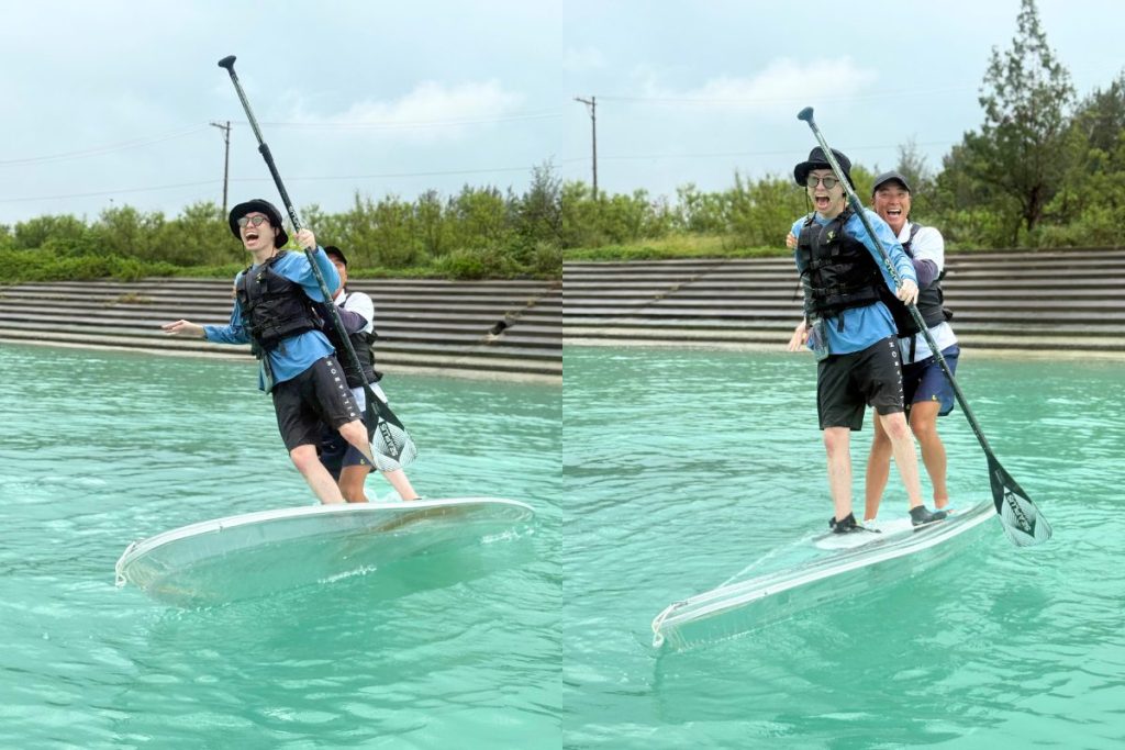 宮古島の海でクリアSUPに立つたくとさんをガイドのしょーだいが後ろから支え、2人で笑いながらバランスを取る様子