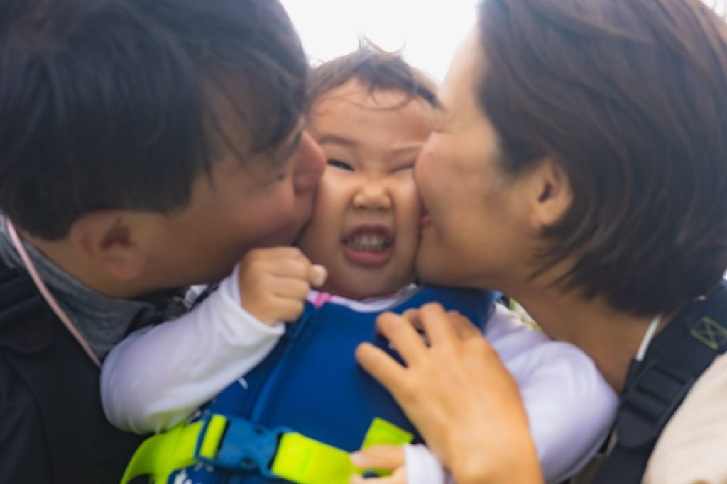 インギャーマリンガーデンでライフジャケットを着た女の子の両頬に、父親と母親がキスをしている笑顔の写真