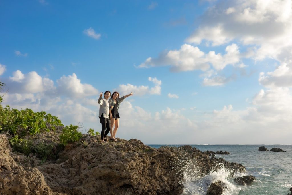 宮古島の青い海を背景に、岩場の上で笑顔でポーズを決めるまあいさん・なつみさん親子