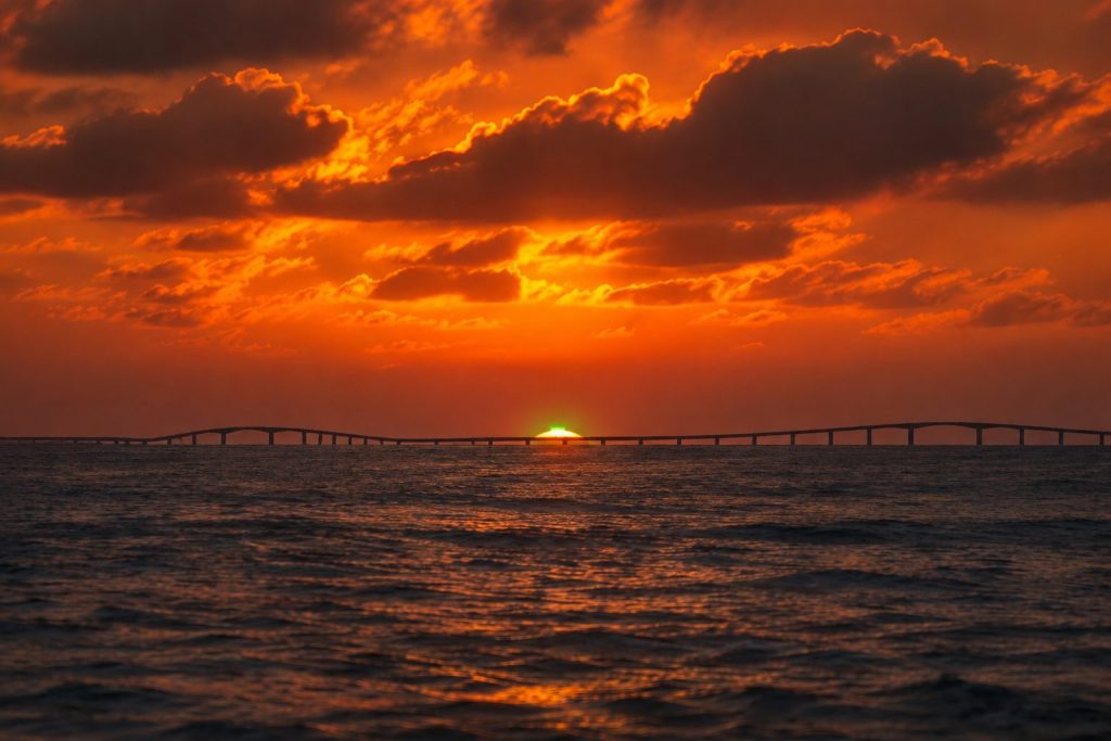 宮古島の伊良部大橋を背景に、水平線へ沈む夕陽が一瞬緑色に輝くグリーンフラッシュの幻想的なイメージ画像
