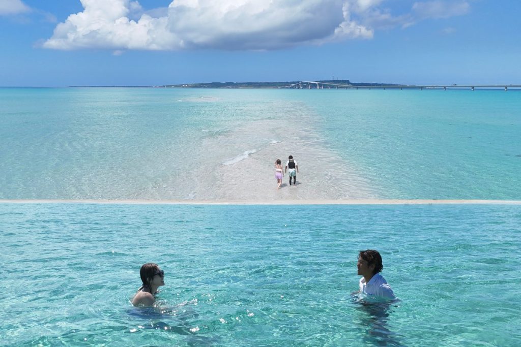宮古島・ユニの浜で、伊良部大橋を背景に浅瀬を歩くかすみさんとガイドの姿と、透明な海の中で向かい合って笑う様子