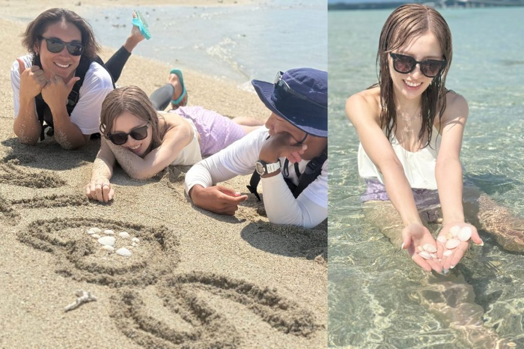 ユニの浜の砂浜でガイドと一緒に寝転ぶかすみさんと、浅く透明な海の中で両手いっぱいの貝殻を見せるかすみさん